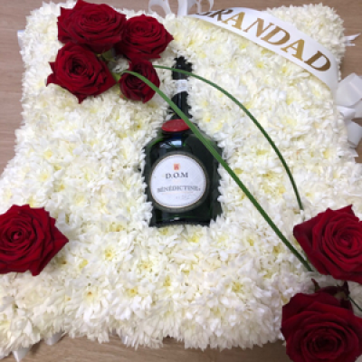 Cushion - Made with white basing chrysanthemums and your loved ones favourite tippel placed in the centre of the display