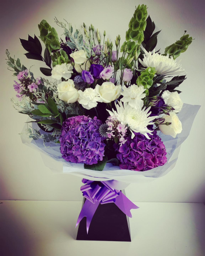 PURPLE HAZE - A large front facing hand tied bouquet in a box of water. This beautiful hand tie is perfect for any occasion with a mix of lilies, roses, hydrangeas and more.