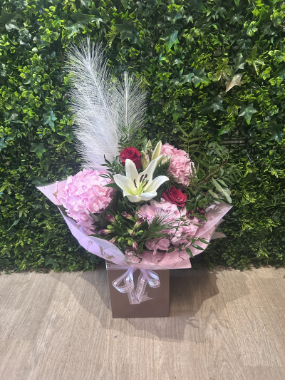 Luxury Pink Lily & Hydrangea Gift Box - An elegant and eye-catching floral arrangement presented in a stylish gift box, perfect for making a lasting impression. This design features soft pink hydrangeas paired with a striking white oriental lily, complemented by rich cerise roses, delicate buds and lush greenery. Finished with decorative feather accents for added height and texture, it offers a modern yet romantic feel.

Beautifully wrapped and tied with coordinating ribbon, this arrangement is ideal for birthdays, anniversaries, celebrations or as a thoughtful “just because” gift. Designed in floral foam, no vase is required — simply place and enjoy.

A luxurious floral gift that combines statement blooms with contemporary presentation.